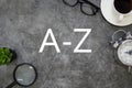 Top view of sunglasses,a cup of coffee, clock,plant, and magnifying glass on grey floor background written with A-Z Royalty Free Stock Photo