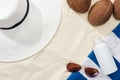 Top view of sunglasses, striped towel, coconuts and white straw hat near white lotion on sand. Royalty Free Stock Photo