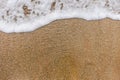 Top view of surface of clean golden sand at sea beach and white foamy wave