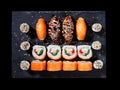 Top view of sushi set with rolls of California, sashimi and maki on a black plate.