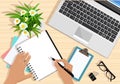 Top view of table with laptop, papers, tablet, flowers, eyeglasses and hands with pen. Modern graphic business workplace.