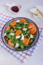 Top view of tangerine salad with mixed leaves, Camembert and walnuts in a grey bowl on cotton chessboard pattern napkin