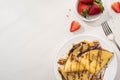 Top view of tasty crepes with chocolate spread and walnuts on plate near bowl with strawberries and fork Royalty Free Stock Photo