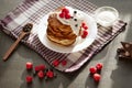 Top view of tasty pancakes with blueberries and raspberries on dark brown table, cup of tea or coffe, wooden spoon with fresh