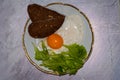 Tasty traditional breakfast with fried egg protein and whole yolk, slices bread with heard shape and greenery Royalty Free Stock Photo