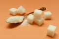 Closeup of teaspoon full of sugar and pile of sugar cubes on the orange background Royalty Free Stock Photo