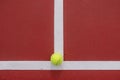 Top view of a tennis ball placed on a surface colored with red and separated with white lines