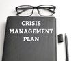 Top view text CRISIS MANAGEMENT PLAN on black book with pen and eye glasses isolated on white background. Royalty Free Stock Photo