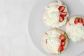 Top view of three Pavlova meringue cakes with fresh strawberry on a white plate on white background with copy space. Homemade
