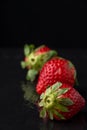 Top view of three strawberries, with selective focus, on wet black stone slate, black background, with reflection, vertical, Royalty Free Stock Photo