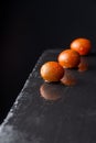 Top view of three wet small kumato tomatoes, with selective focus, on black slate with reflection, black background, vertical Royalty Free Stock Photo