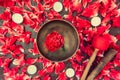 Top view tibetan singing bowl with floating inside in water red peony flower. Burning candles and petals on the black stone backgr