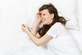 Top view of tired stressed crying young brunette woman lying in bed with white sheet, pillow, blanket. Shocked Royalty Free Stock Photo