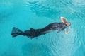 Top view to a beautiful sexy young woman floating like a mermaid fish, wrapped in black cloth dress in turquoise blue water of the