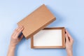 Top view to female hands open empty brown cardboard box on light blue background. Mockup parcel box. Packaging, shopping