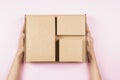 Top view to stack of cardboard boxes in female hands. Blank brown parcel boxes on pastel pink background. Packaging Royalty Free Stock Photo