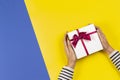 Top view to woman hands holding gift present box decorated with bow on yellow and blue background Royalty Free Stock Photo