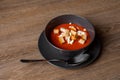 Top view of toothsome tomato soup with sour cream and croutons in black bowl on plate with spoon on brown wooden table. Royalty Free Stock Photo