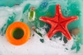 Top view on toy ocean in aquarium. Top view on blue watr with white foam, red starfish, stone, small glass bottle and round orange Royalty Free Stock Photo