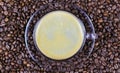 Top view on transparent glass cup, saucer and handle with black coffee whitecap crema, blurred roasted coffee beans background Royalty Free Stock Photo