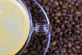 Top view on transparent glass cup, saucer and handle with black coffee whitecap crema, blurred roasted coffee beans background Royalty Free Stock Photo