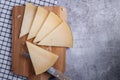 Top view of triangle pieces of cured Manchego cheese and a sharp knife on a wooden food board