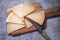 Top view of triangle pieces of cured Manchego cheese and a sharp knife on a wooden food board