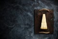 Top view of triangular piece of hard cheese on wooden cutting board