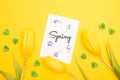 Top view of tulips, card with spring lettering and decorative green hearts on yellow background.