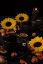 Top view of two black tea cups on table with black tablecloth with nuts, yellow flowers