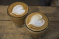 Top view of two Cappuccino cups with artistic heart shape, on a brown wooden table