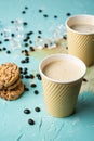 Top view of two cardboard cups with cappuccino coffee on blue table, spilled coffee, coffee beans