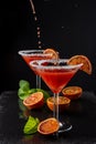 Top view of two cocktail glasses with drops of blood orange martini, half orange and mint, on black background, vertical Royalty Free Stock Photo