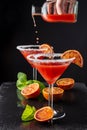 Top view of two cocktail glasses with unfocused bottle serving drops of blood orange martini, half orange and mint, on black backg Royalty Free Stock Photo