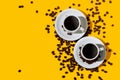 Top view of two coffee cup over a bright yellow color background and many beans spilled around Royalty Free Stock Photo