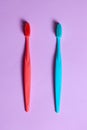 Top view on two colored tooth brushes, coral red and blue one, laying down on lilac pink background. Royalty Free Stock Photo