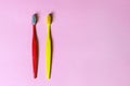 Top view on two colored tooth brushes, red and yellow, laying down on lilac pink background.