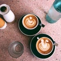 Top view of two cups of cappuccino with bottle of water and glass cup on granite table