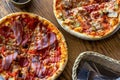 Top view of two fresh baked homemade sliced pizzas with cheese and ham topping served with kitchenware on wooden background. Royalty Free Stock Photo