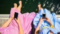 Top view of two girls sitting on the pier barefooted with feet in the sea and smartphones in their hands Royalty Free Stock Photo