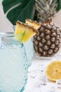 Top view of two glasses with lemon juice with pieces of pineapple on white wooden table with half a lemon, ice and pineapple, on w