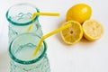 Top view of two glasses with lemon juice with yellow straw and half lemons, selective focus, on white table, horizontal, Royalty Free Stock Photo