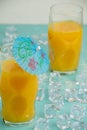 Top view of two glasses with orange juice, with blue umbrella, on blue table with ice, selective focus, Royalty Free Stock Photo