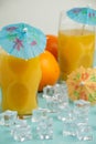 Top view of two glasses with orange juice, decorated with blue umbrellas, on blue table with ice and oranges, selective focus, Royalty Free Stock Photo