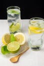 Top view of two glasses of water with lemon and lime slices with ice cubes on white wood, with wooden spoon, plate with half lemon Royalty Free Stock Photo