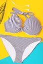 Top view of two pieces striped blue and white swimming suit on blue and yellow pastel background. Copy space. Concept of