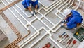 Top view of two plumbers installing a complex system of white and copper pipes on a concrete floor. Royalty Free Stock Photo