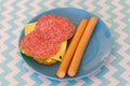 Top view of two sausages next to bread with cheese and salami on a blue plate in soft focus Royalty Free Stock Photo