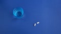 Top view of two white round medical pills, vitamins, a beautiful blue glass with clean water. Royalty Free Stock Photo