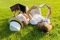 Top view, two young female students reading books lying on green grass.